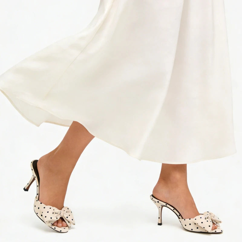 Polka dot high-heeled shoes worn with a white dress on a white background