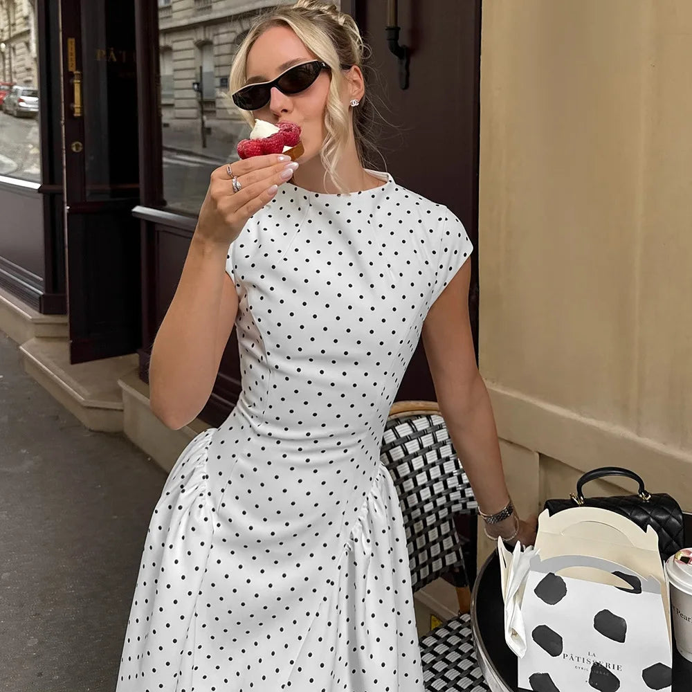 Woman in a polka dot dress eating ice cream on a city street.