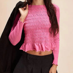 Person wearing a pink textured long-sleeve top with ruffled details on a beige background
