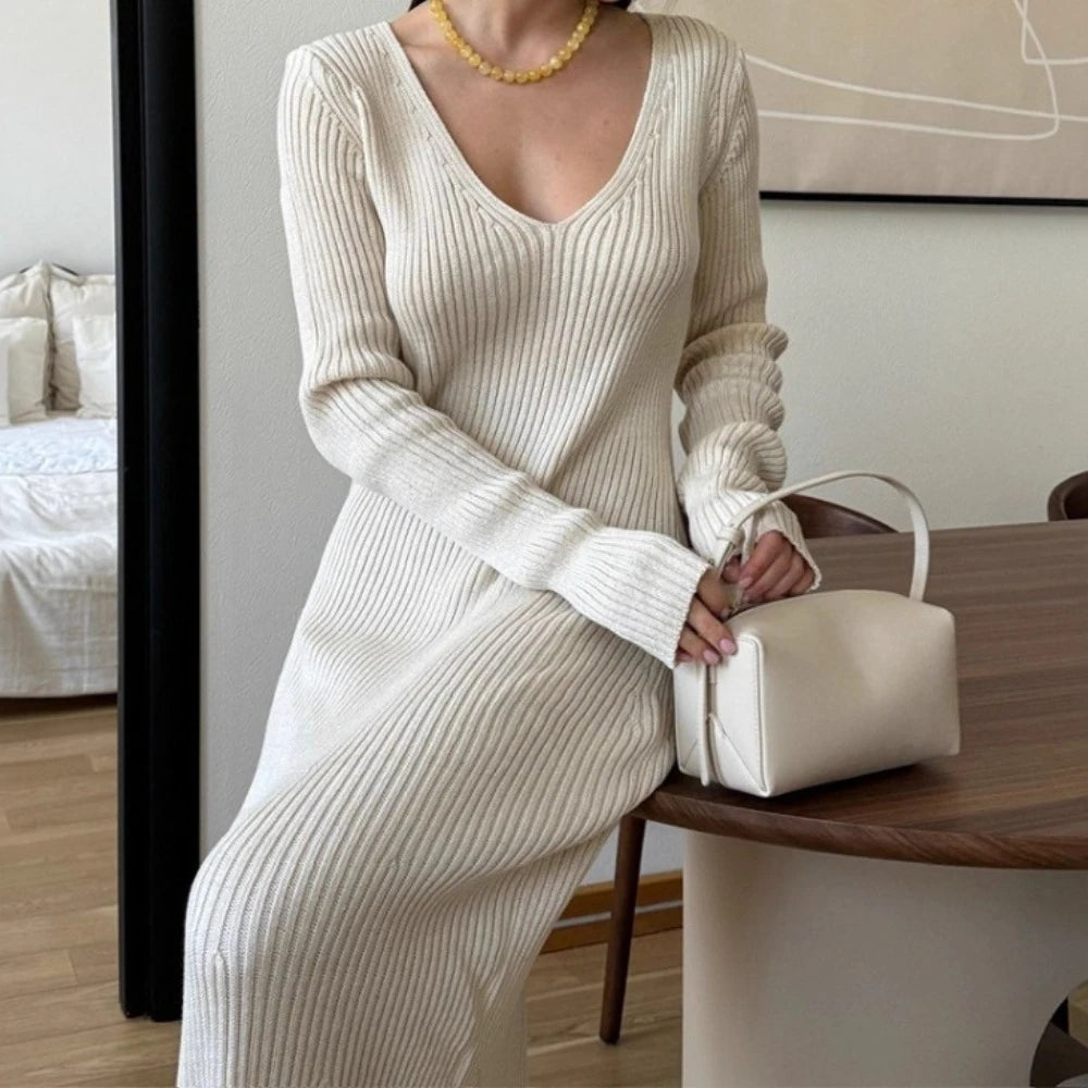 Person wearing a cream ribbed dress holding a matching handbag in an indoor setting.