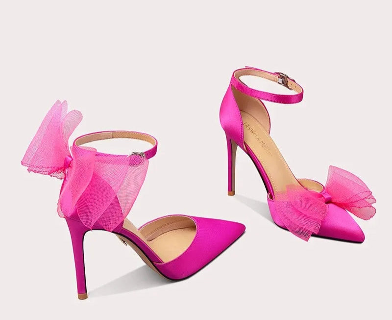 Pink high-heeled shoes with bow details on a light gray background