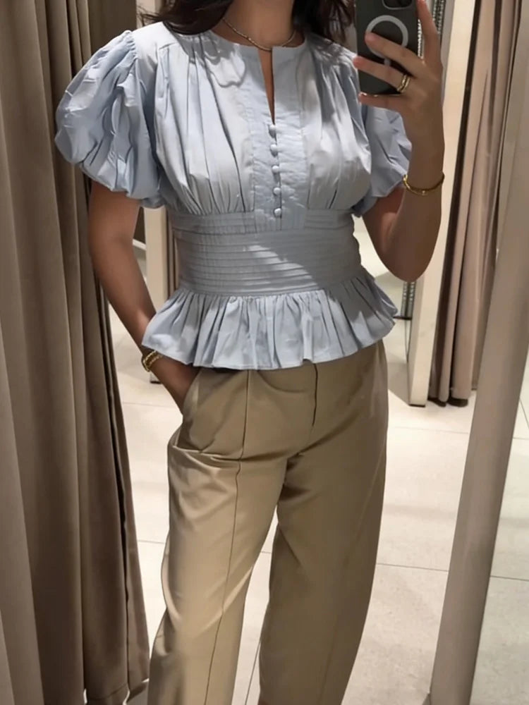 Person wearing a light blue ruffled blouse and beige pants in a mirror selfie.