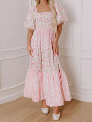 Woman wearing a pink floral dress against a white paneled wall.