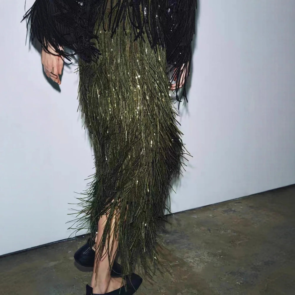Person wearing a long, dark green feathered dress with black feathers on a plain background