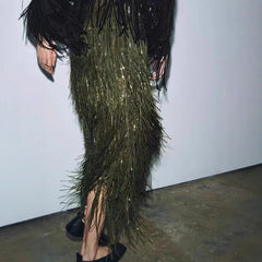 Person wearing a long, dark green feathered dress with black feathers on a plain background