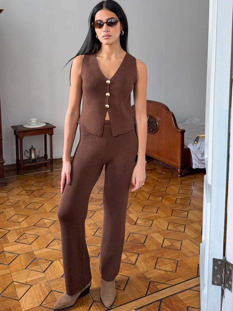 Woman wearing a brown outfit in a room with wooden flooring and a bed.