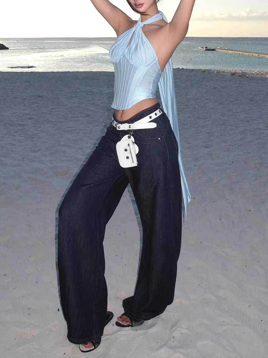 Person on a beach wearing a light blue halter top and dark pants with a white bag.