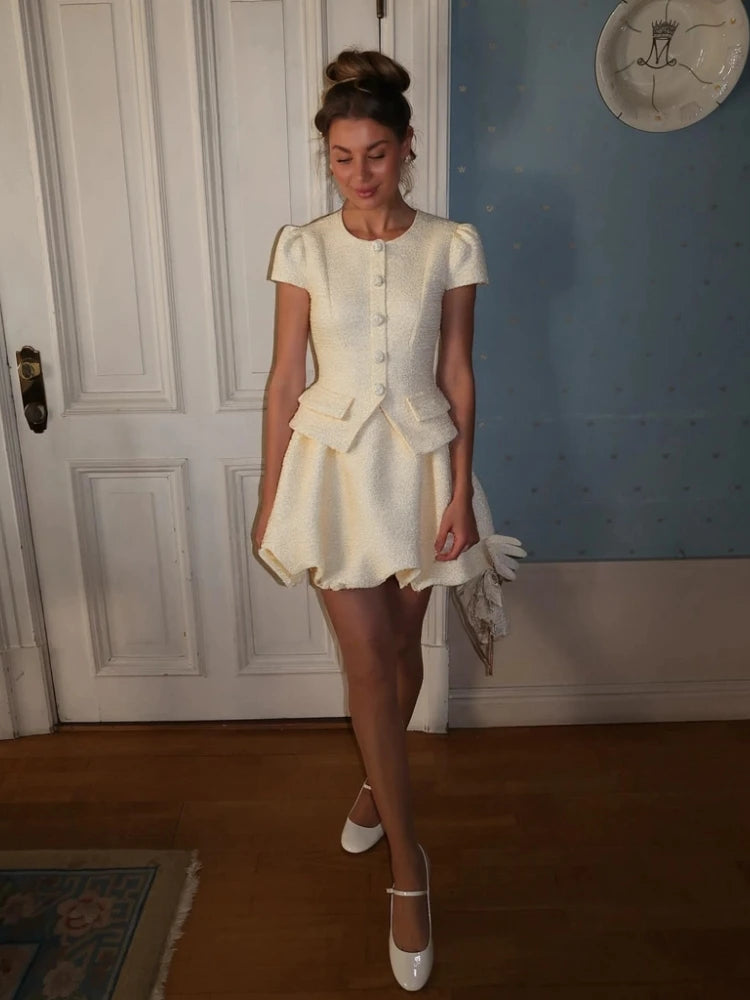 Woman in a white outfit standing in a room with a blue wall and white door.