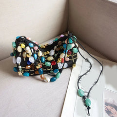 Black shoulder bag decorated with a mosaic of colorful stones and gold beads.