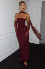 Model in strapless burgandy ankle-length sheath dress with chiffon scarf and backless design.