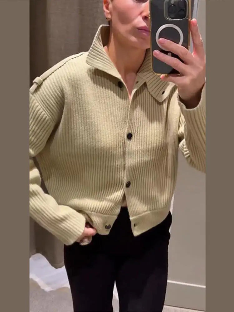 Person wearing a light green ribbed sweater taking a mirror selfie.