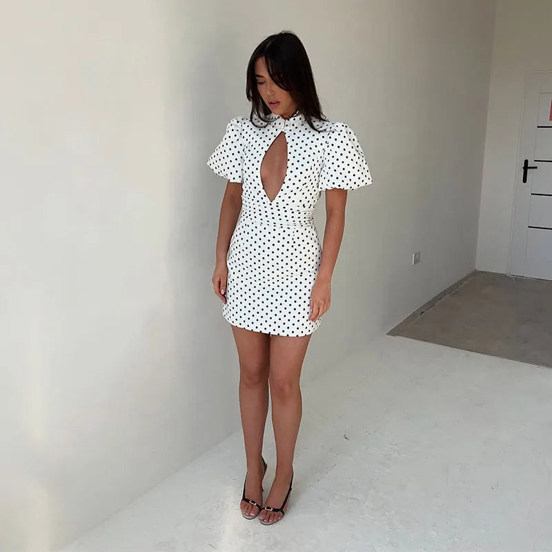 Woman wearing a white dress with black polka dots in a minimal room.