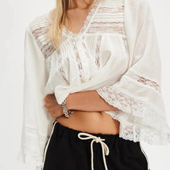 Woman wearing a white lace cover-up over a black swimsuit with a plain background