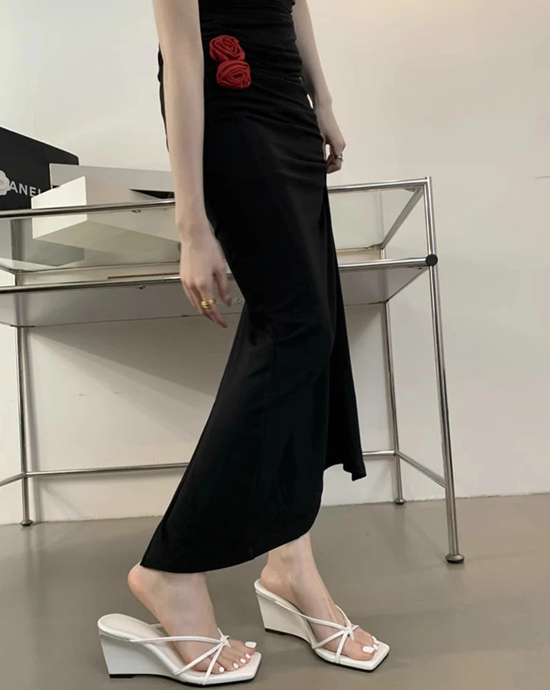 Person wearing a black dress with a red rose detail, standing in an indoor setting.