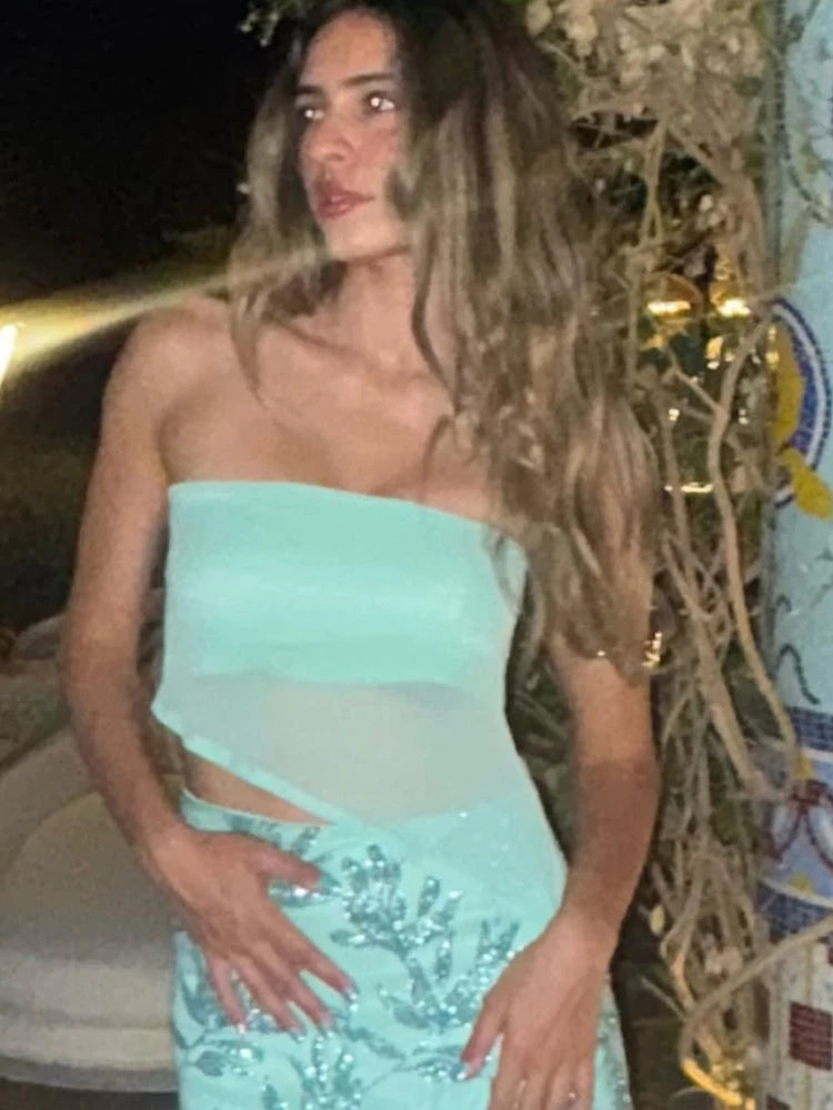 Woman wearing a light blue strapless top and sequined skirt outdoors at night.