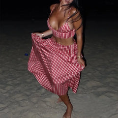 Woman wearing a red and white striped print two-piece set with a V-neck crop top and flowing maxi skirt on a beach at night.