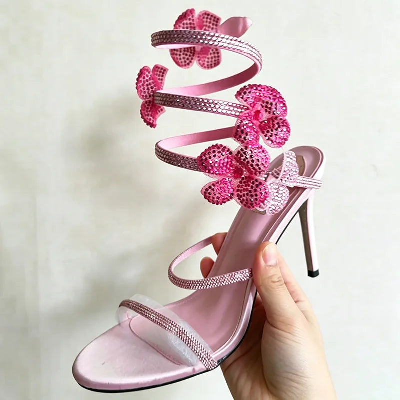 Close-up of a hand holding a pink crystal flower ankle strap stiletto heel