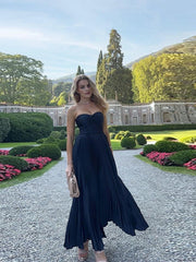 Woman in a navy strapless gown standing in a garden with manicured hedges and trees.