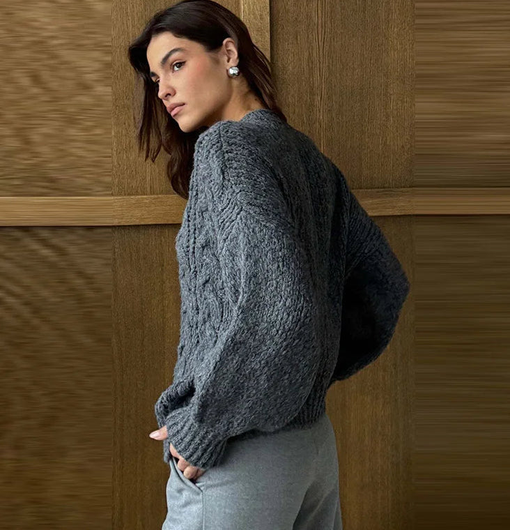 Woman wearing a gray sweater against a wooden paneled wall