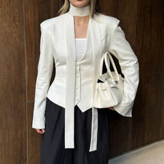 Person wearing a white blazer and holding a matching handbag against a wooden background
