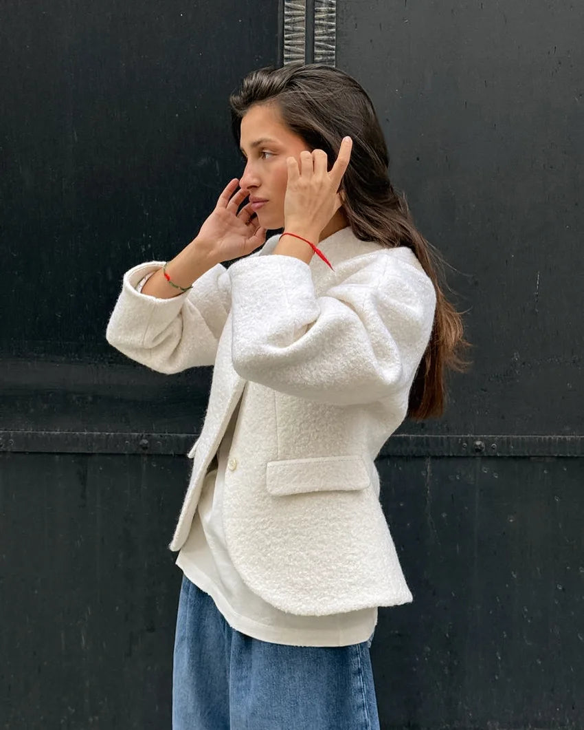 Woman wearing a white textured jacket and blue jeans against a black background