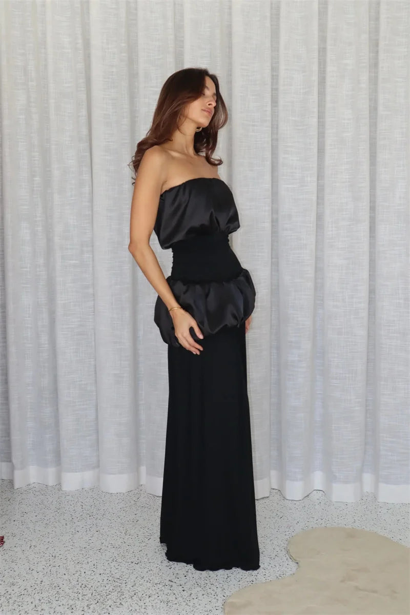 Woman wearing a black strapless gown against a white curtain background
