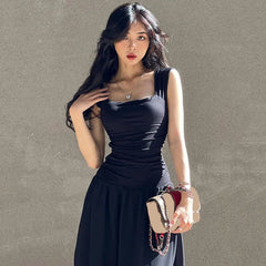 Woman in a black dress holding a beige clutch against a gray background