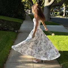 Woman in a floral dress twirling on a sidewalk with trees and grass in the background