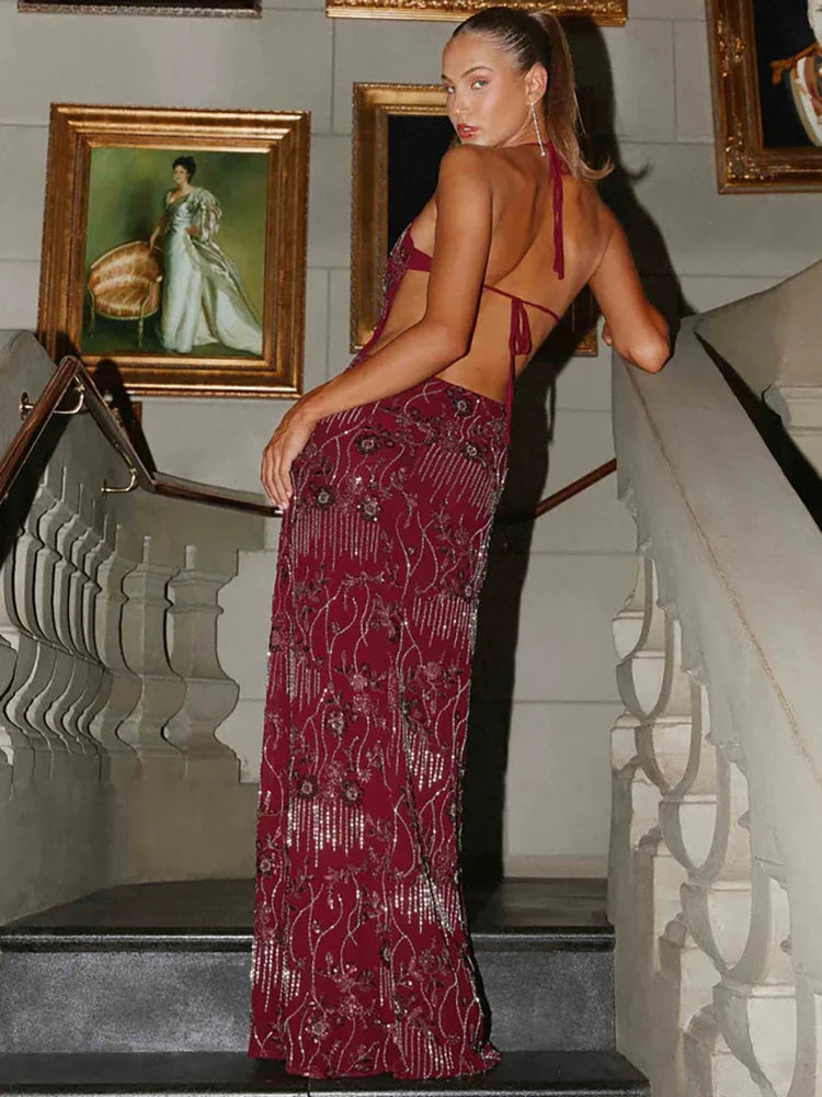 Woman in a burgundy evening gown standing on a staircase with decorative wall art in the background.