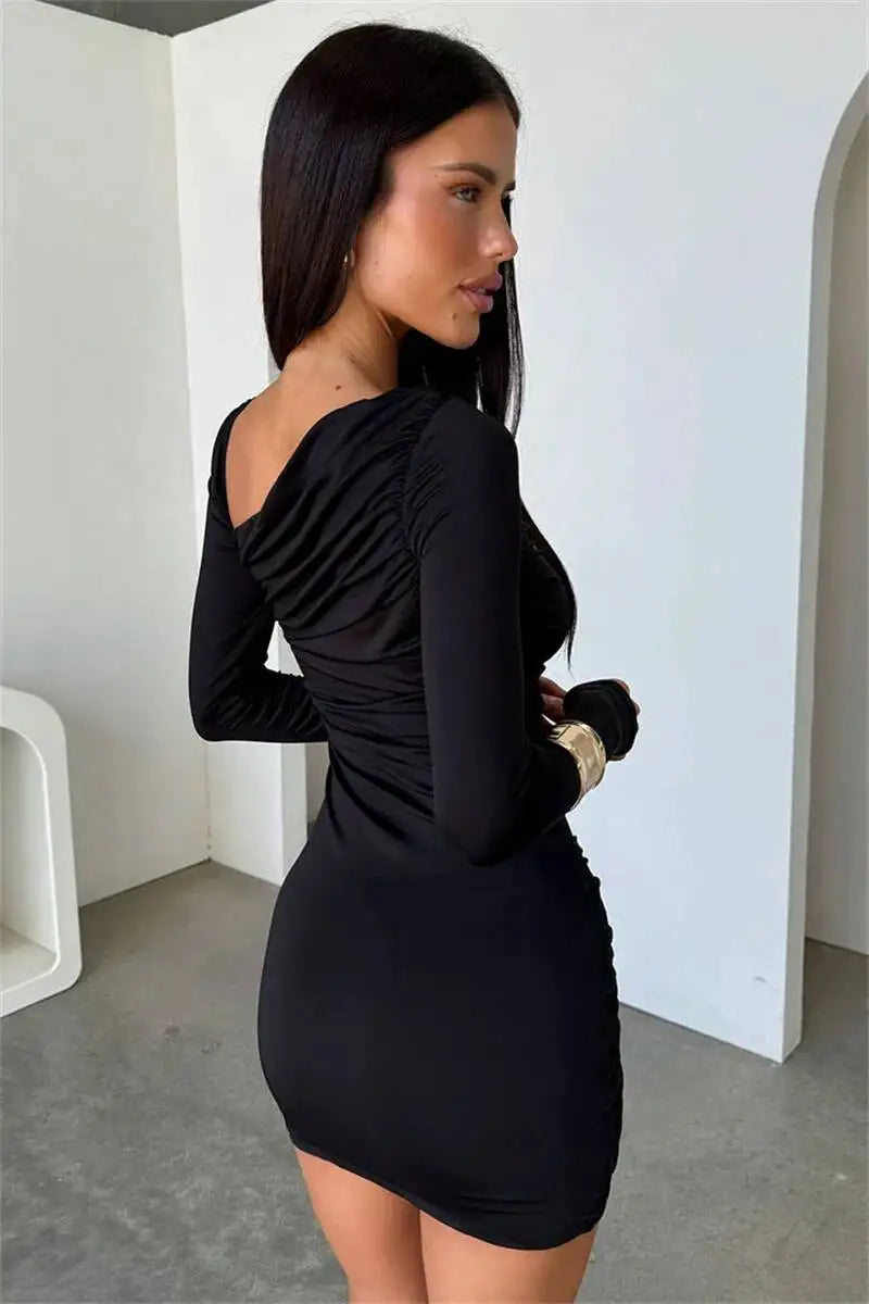 Woman wearing a black dress standing in a minimalistic room with white walls and gray floor.