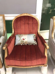 Red upholstered chair with gold accents and a decorative pillow in a showroom setting.