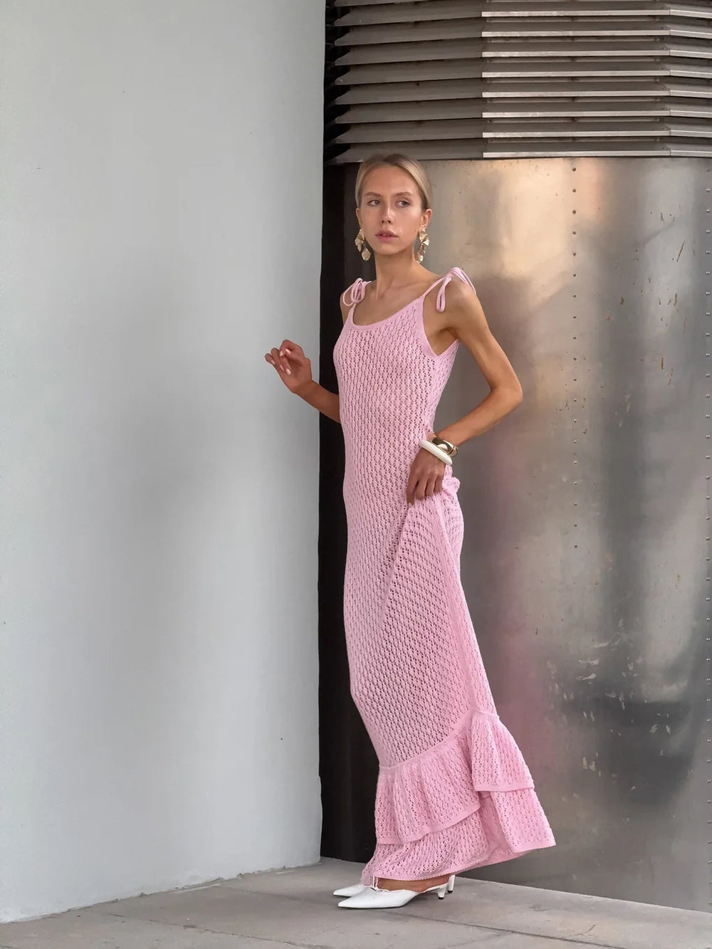 Woman wearing a pink dress standing against a metallic wall.
