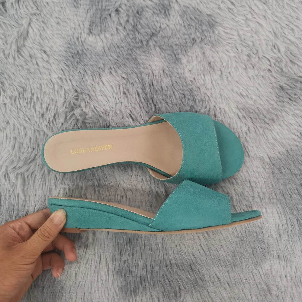 Turquoise wedge heel open toe mules on a grey fluffy surface