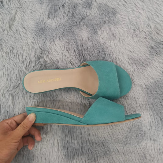 Turquoise wedge heel open toe mules on a grey fluffy surface