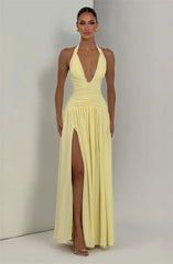 Woman wearing a yellow halter neck gown with a high slit on a plain background