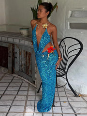 Woman in a blue sequin dress standing in a room with a black chair and white wall.