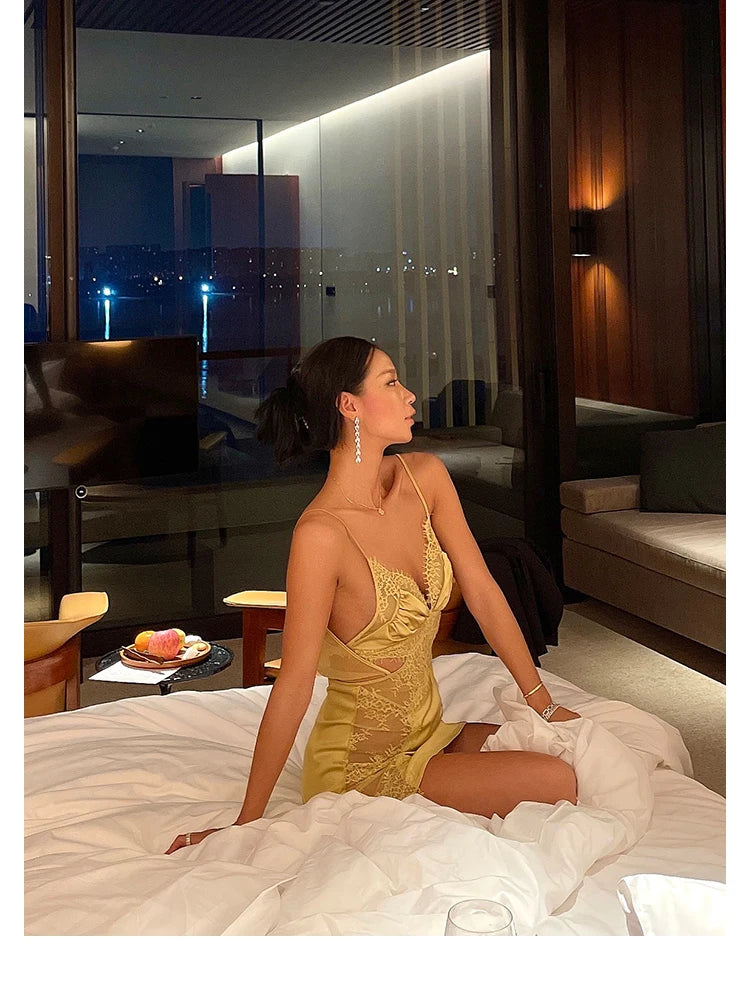Woman in a gold dress sitting on a bed in a luxurious room with city lights visible through the window.