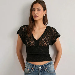 Woman wearing a black lace top and blue jeans against a plain background