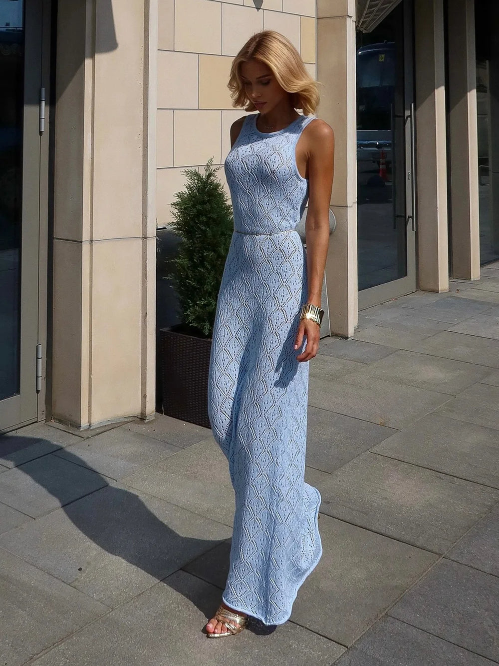 Woman in a light blue lace dress standing on a sidewalk.