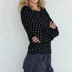 Person wearing a black long-sleeve top with white polka dots and dark jeans against a light background