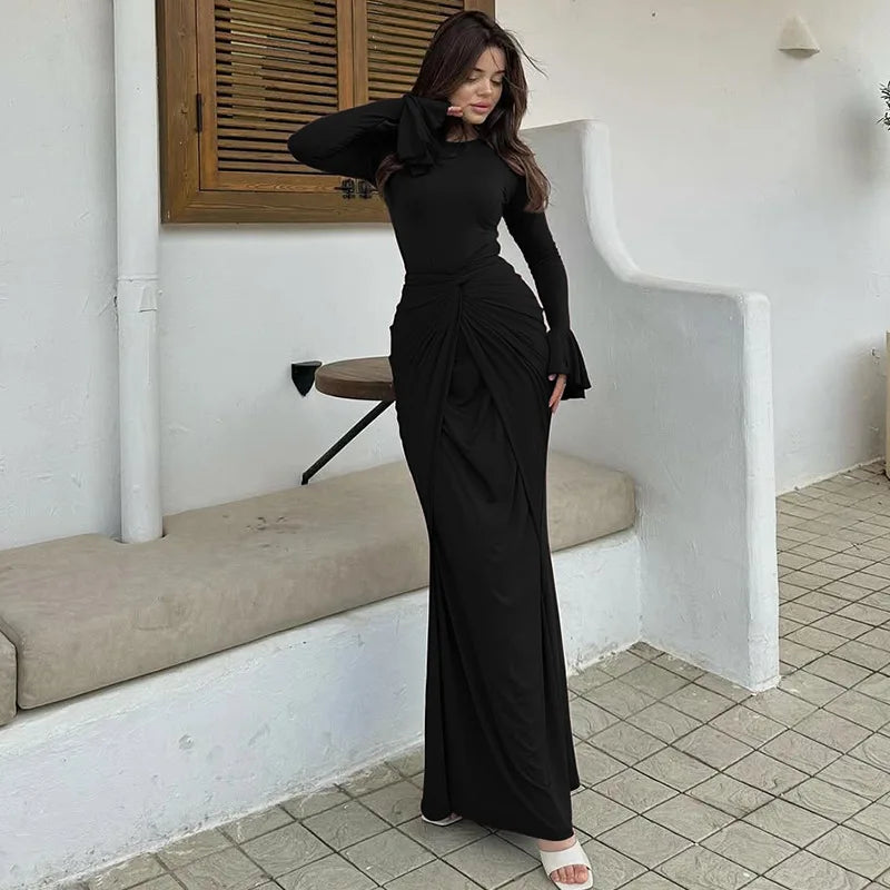 Woman in a black dress standing in a minimalistic room with white walls and tiled floor.