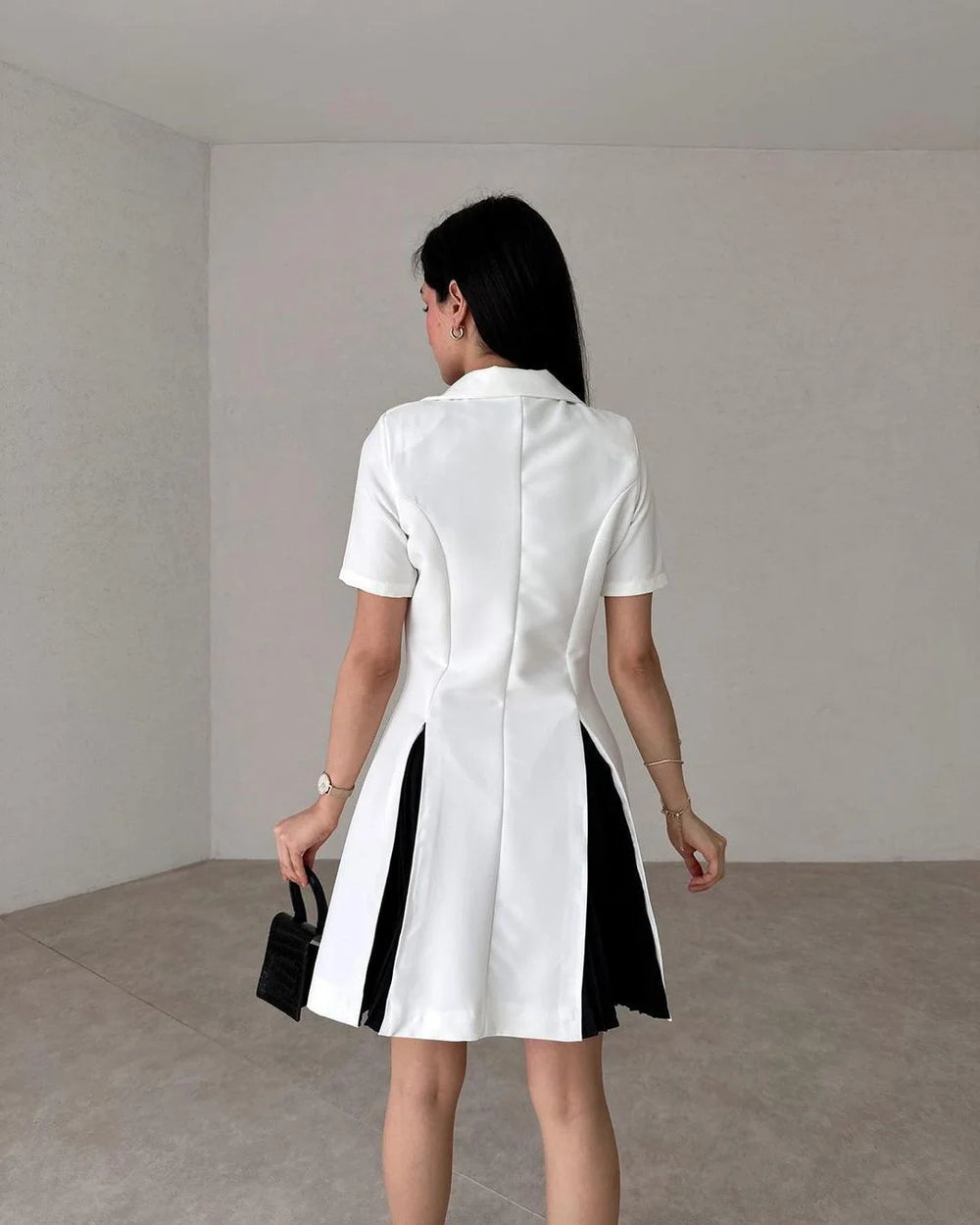 Woman wearing a white dress with black accents in a minimalistic room.