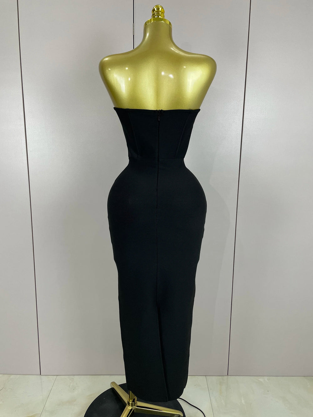 Black evening gown on a gold mannequin against a white wall