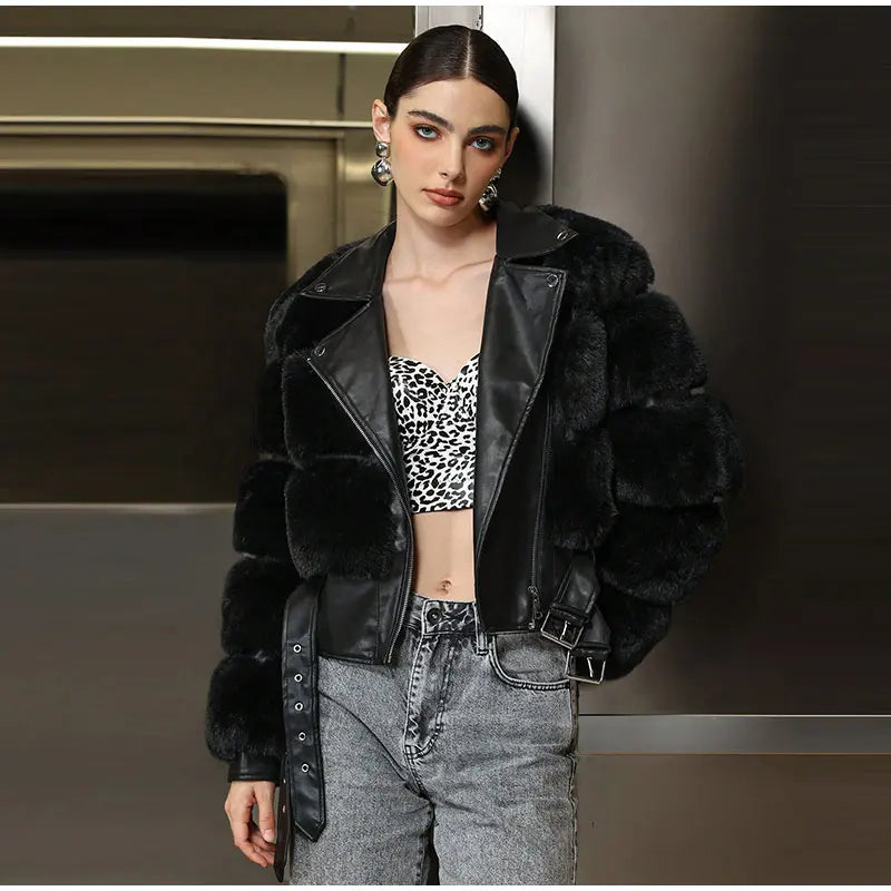 Woman wearing a black fur jacket over a leopard print top and gray pants.