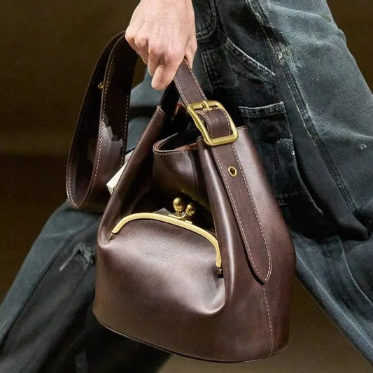 Brown leather handbag with gold hardware held by a person wearing jeans.