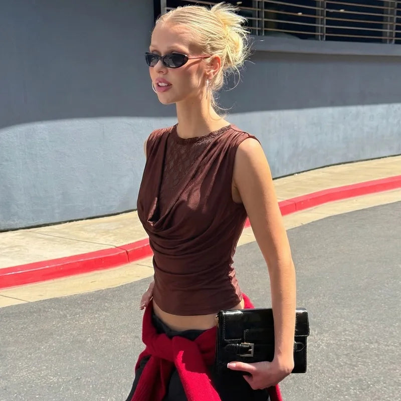 Woman in a brown sleeveless top and red skirt holding a black clutch on a street.