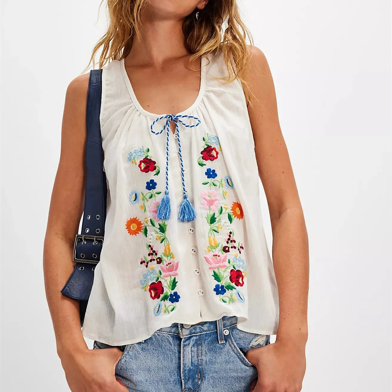 Woman wearing a white sleeveless top with colorful floral embroidery on a plain background