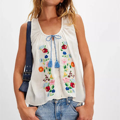 Woman wearing a white sleeveless top with colorful floral embroidery on a plain background