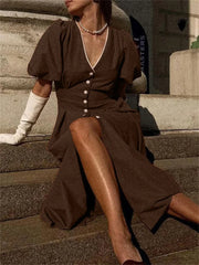 Woman in a brown dress sitting on stone steps wearing white gloves.
