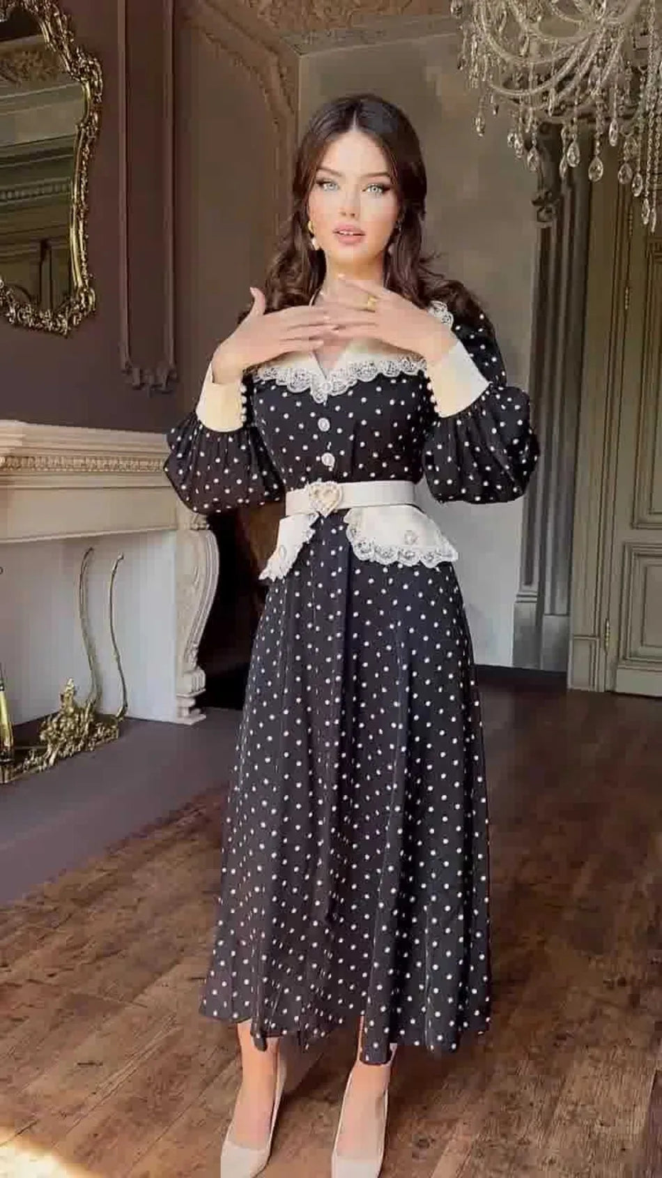 Woman wearing a black polka dot dress with white lace details in an elegant room.
